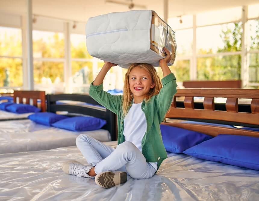Kind sitzt auf Bett mit Matratzentopper